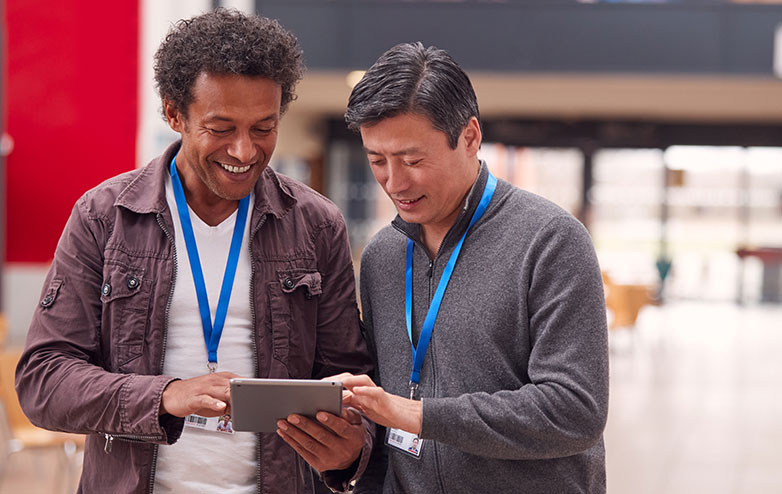 Two smiling men look at a smart tablet together