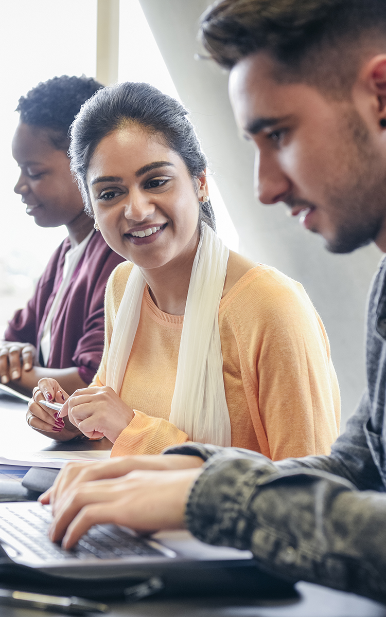 Three students work together on a laptop