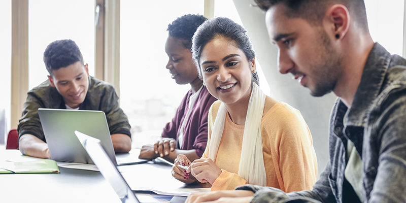 Three students work together on a laptop