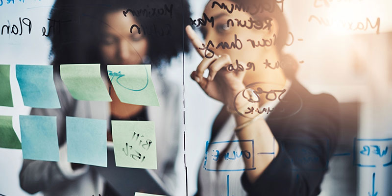 Two women discuss items on a whiteboard