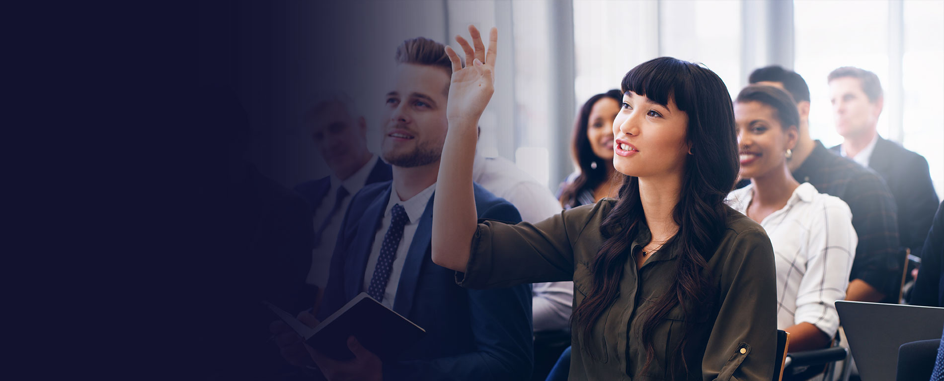 A woman raising her hand in a room full of adult students