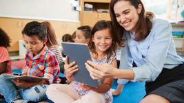 A smiling teacher and young student look at a smart tablet together.