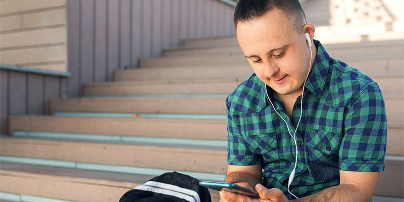 A man sitting on steps outdoors and using a smartphone.