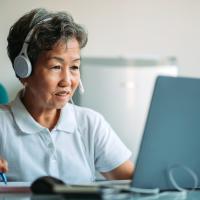 Asian smiling mature businesswoman using laptop with headset 