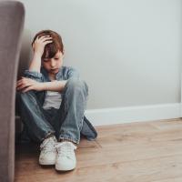 Young boy holding head and sitting on floor