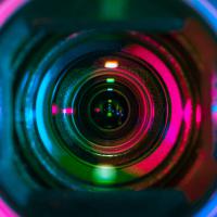 Closeup of a video camera lens, reflecting multicolored stage lights