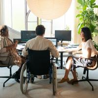 Man in wheelchair at office desk with two female co-workers