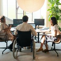Man in wheelchair at office desk with two female co-workers