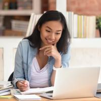 female working in an office in front of a laptop writing on a note pad