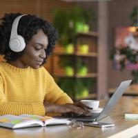 Woman with headphones working on laptop with coffee and open book