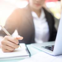 Woman working on laptop while writing in notebook