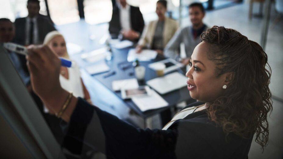 Woman writing on board with co-workers looking