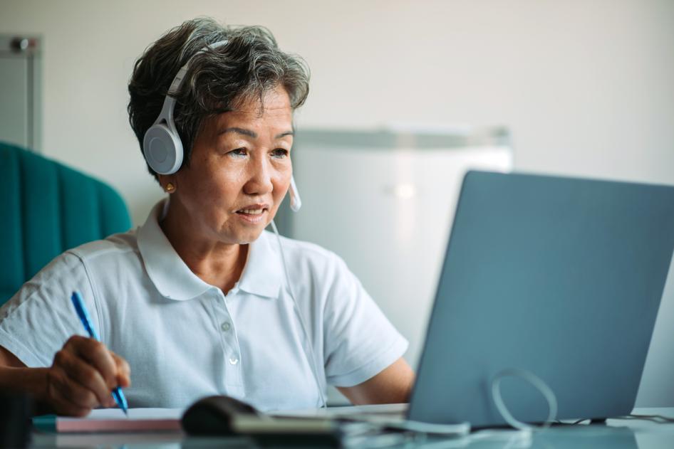 Asian smiling mature businesswoman using laptop with headset 