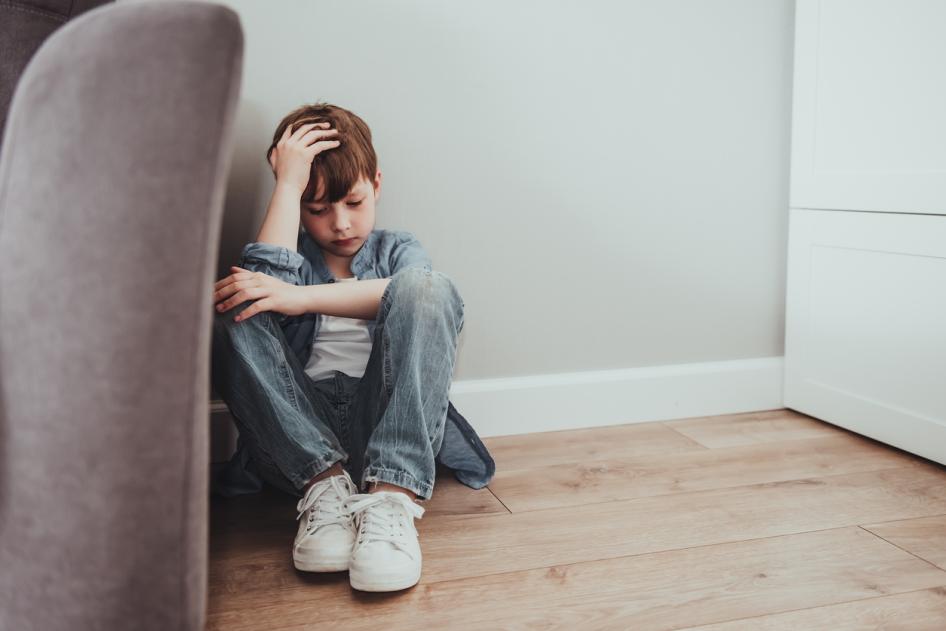 Young boy holding head and sitting on floor