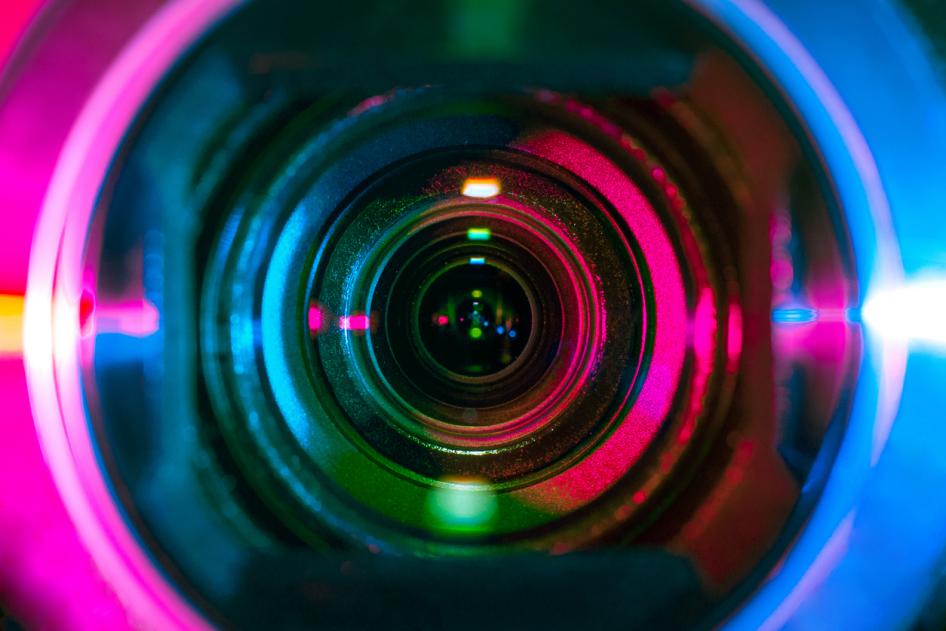 Closeup of a video camera lens, reflecting multicolored stage lights