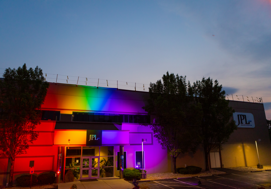 Photo of the JPL building at night, illuminated by rainbow lights