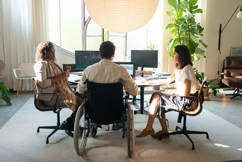 Man in wheelchair at office desk with two female co-workers