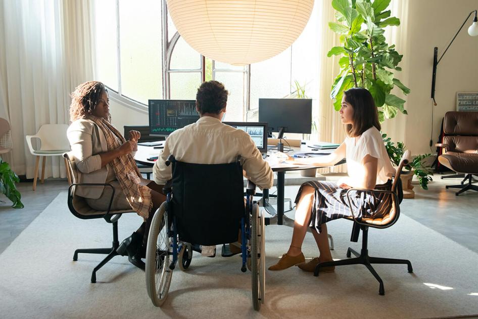 Man in wheelchair at office desk with two female co-workers