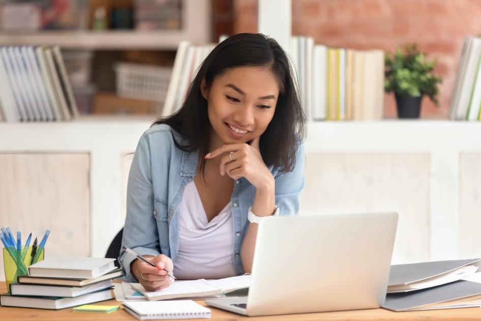 female working in an office in front of a laptop writing on a note pad