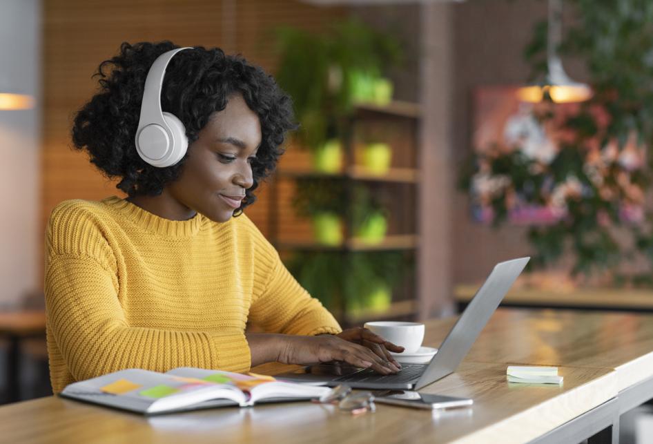 Woman with headphones working on laptop with coffee and open book