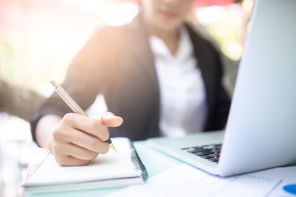 Woman working on laptop while writing in notebook