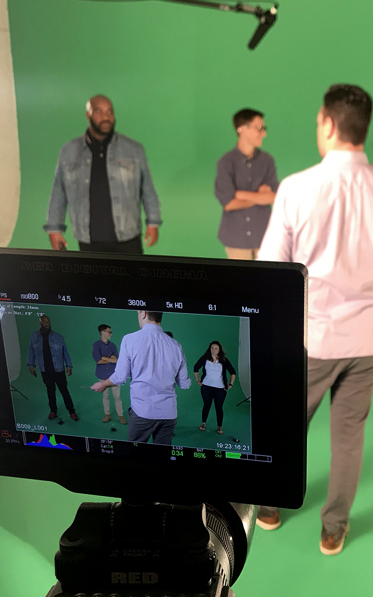 Several people in front of a green screen, being filmed with a video camera.