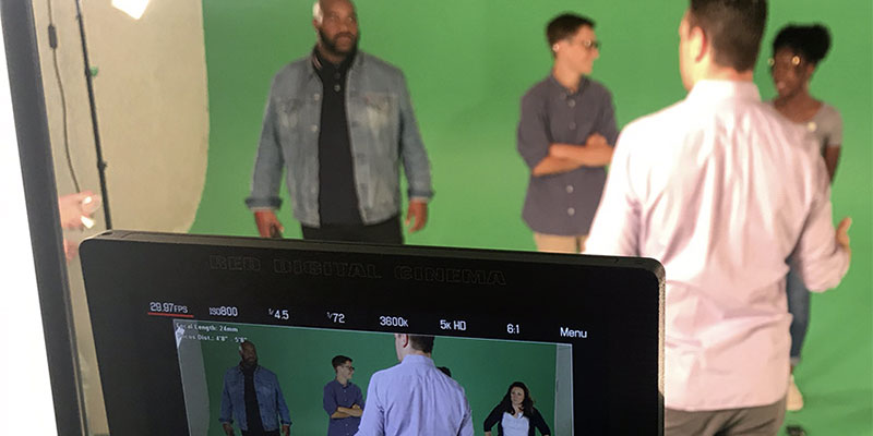 Several people in front of a green screen, being filmed with a video camera.