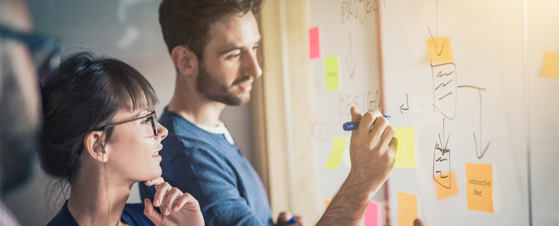 Two people writing on a glass whiteboard